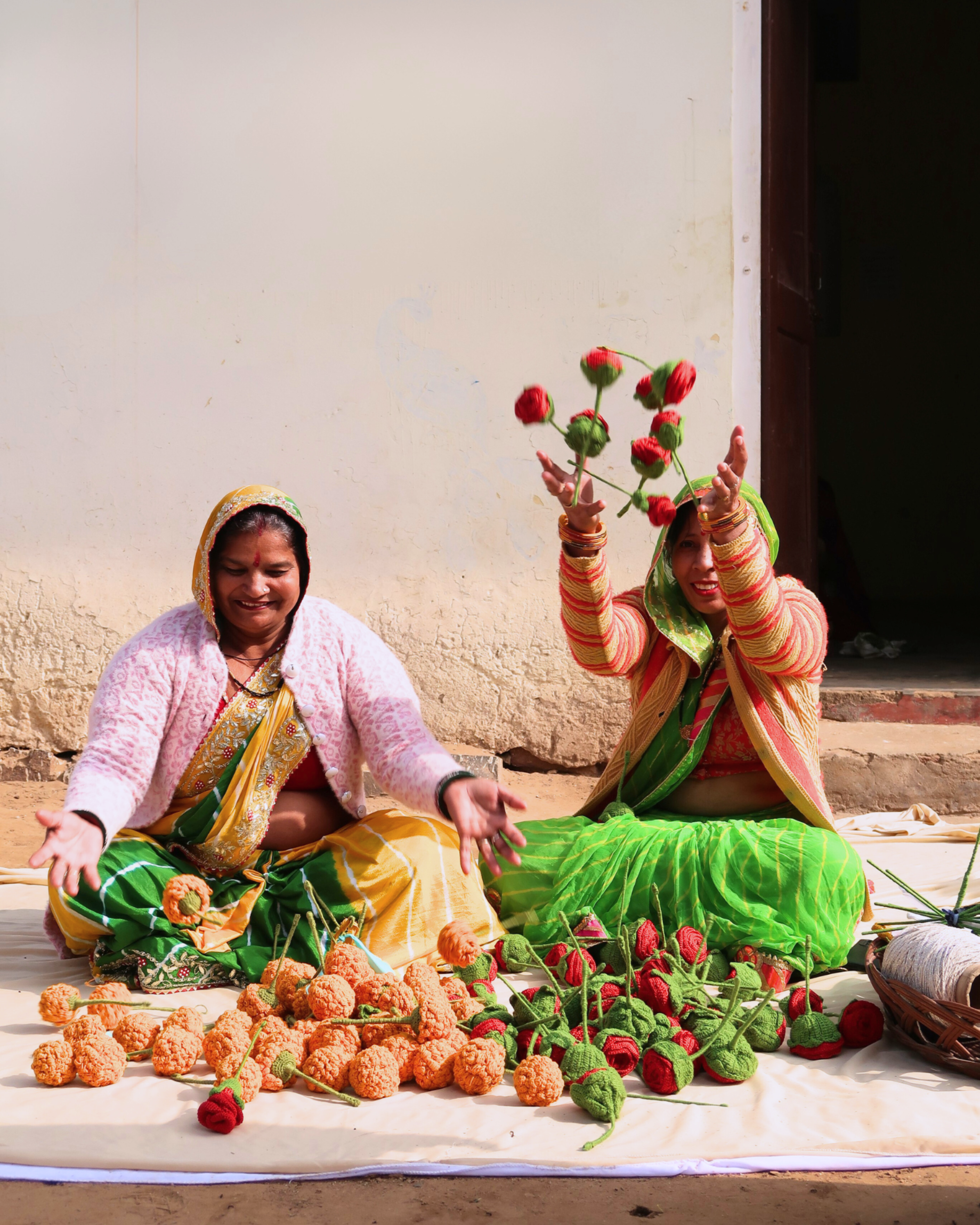 Two women sitting on the ground with flowers and a basket, wearing colorful traditional attire. Meet the makers — crochet flowers handmade by Kalaa Sakhi women artisans India